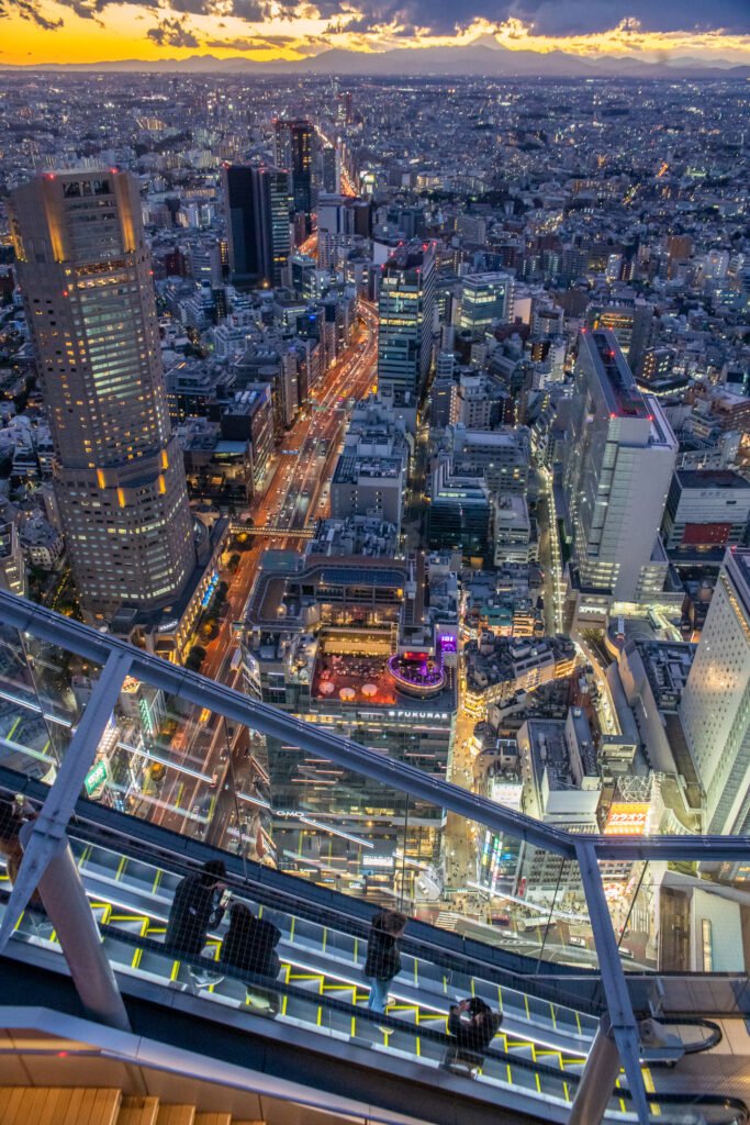 escalator panoramique shibuya sky tokyo.jpg Vue depuis l'escalator vitré du Shibuya Sky surplombant les lumières de la ville de Tokyo à la tombée de la nuit.